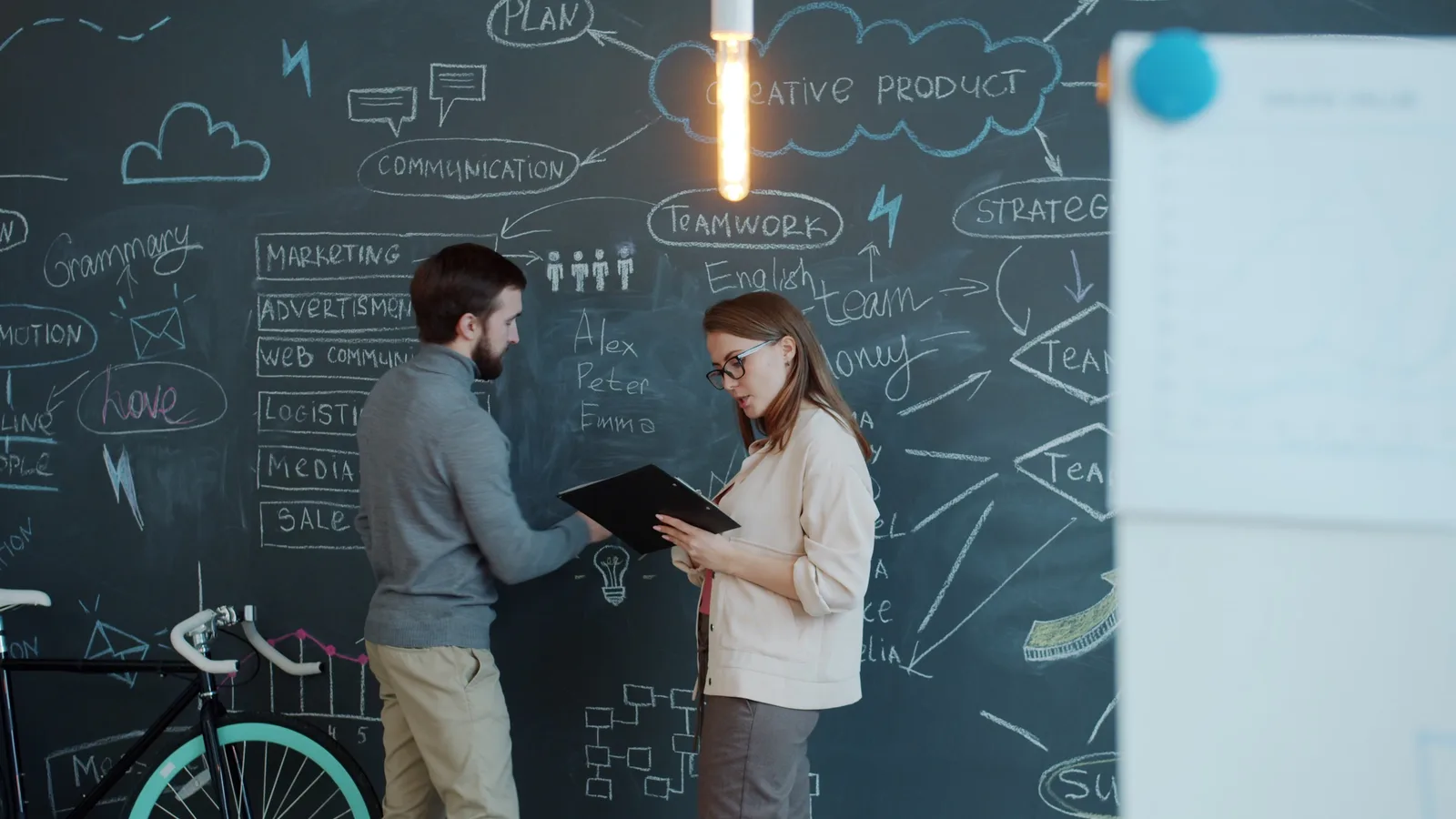 Two professionals discussing creative ideas on a chalkboard in an office.