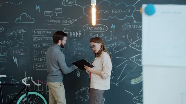 Two professionals discussing creative ideas on a chalkboard in an office. B2B content marketing agency UK: how to choose a specialist