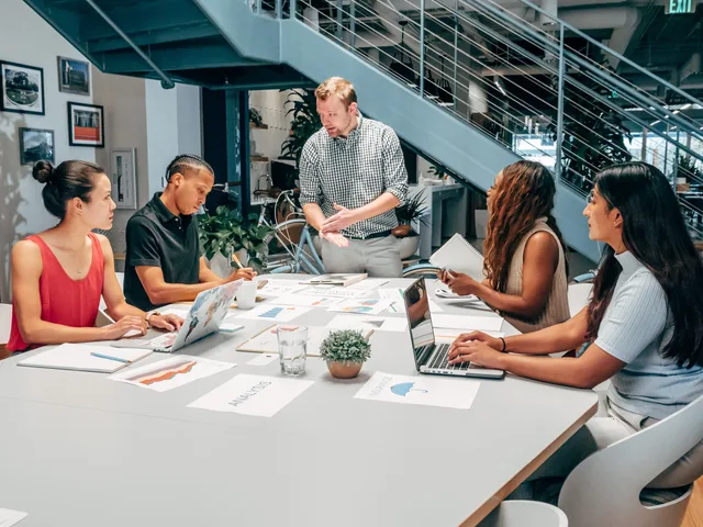A diverse group of colleagues collaborating on a project in a modern office setting with laptops and documents. Buyer personas for content agencies in England